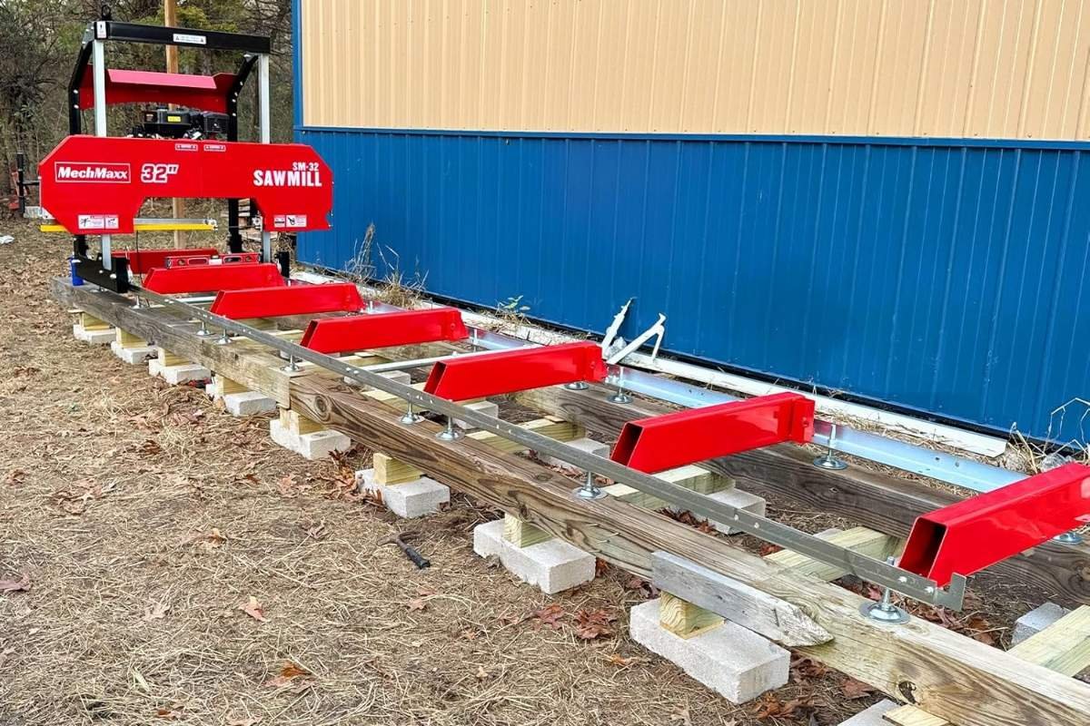 MechMaxx SM-32 sawmill track laid out on blocks beside a metal shed